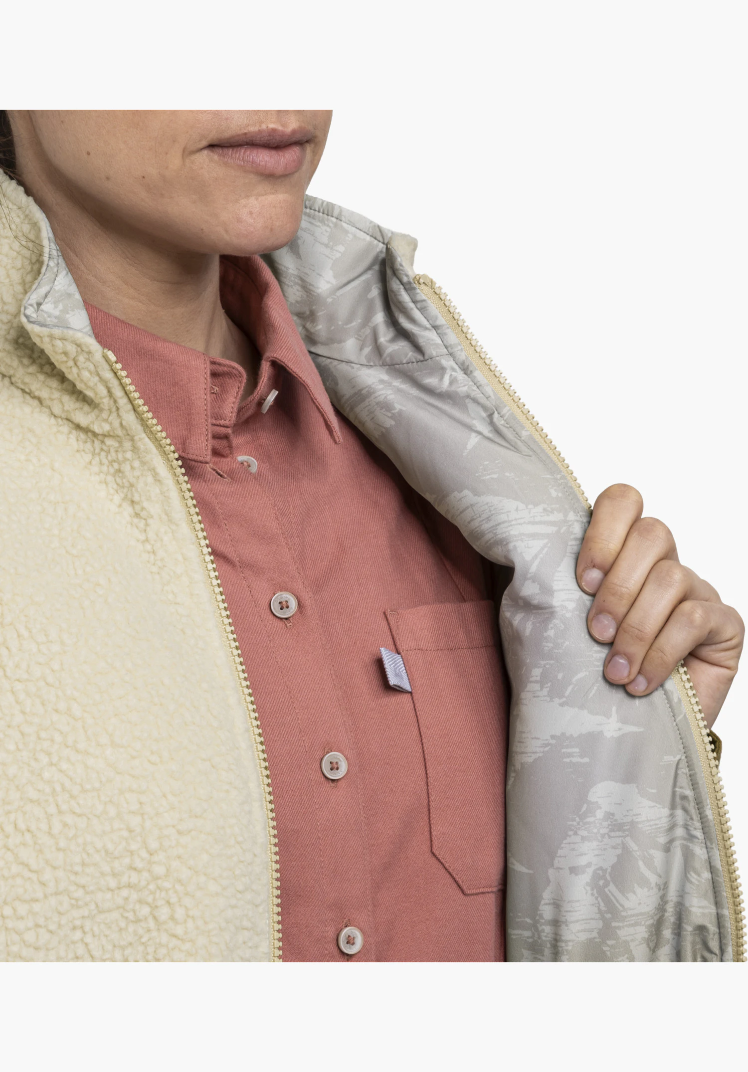 Vest Style Purga WMN in beige met een ritssluiting en een bedrukte voering die door een hand wordt opengehouden in een close-up tegen een witte achtergrond.